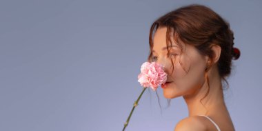 Stüdyo güzelliği, yüzünde pembe bir çiçek tutan parlak tenli şık bir mankenin fotoğrafı. Kopya alanı ile yenilenmiş kompozisyon, cilt bakımı, moda ve kozmetik markalaşma için ideal.