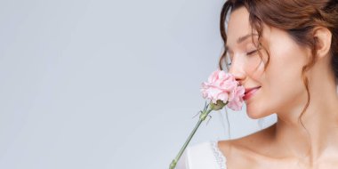 Yüzüne yakın pembe bir çiçek tutan dingin bir kadını gösteren rahatlatıcı bir afiş. Parlak cildi ve kapalı gözleriyle cilt bakımı, kozmetik ürünleri ve sağlıklı markalaşma için mükemmel..