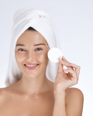 Kafasında havlu olan beyaz bir kadın gülümsüyor ve elinde pamuk tutuyordu. Temiz ve taze cilt konsepti spa, güzellik reklamları, sağlık kampanyaları ve yüz bakımı promosyonları için idealdir..