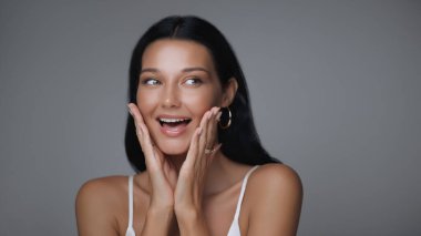 Yüzünde elleri ile gülümseyen neşeli bir kadın heyecan ve mutluluğu ifade ediyor. Reklam kampanyalarında güzellik, cilt bakımı ve yaşam tarzı kavramları için mükemmel..