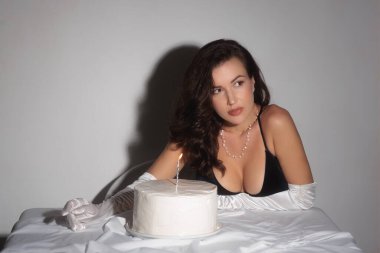 Siyah elbiseli zarif bir kadın masanın üzerinde bir pastayla poz veriyor. Sahne sofistike ve kutlama dolu, etkinlik promosyonları, lüks yaşam tarzı içeriği ve parti temalı görseller için mükemmel..