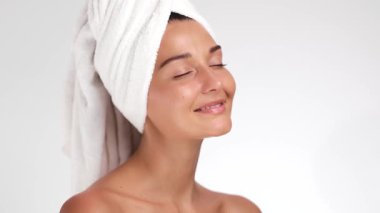 Huzurlu bir kadın havluyla sarılıyken kusursuz, parıldayan tenine nazikçe dokunuyor. Cilt bakımı, güzellik ya da kendi kendine bakım kampanyaları için ideal rahatlama ve ışıltı odaklı. 