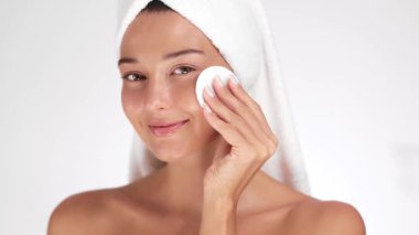 Havluya sarılmış yeni yüzlü bir kadın nazikçe pamuk yastıkla cilt bakımı, güzellik, kendine bakım ve cilt bakımı yapar. Sağlık, kozmetik ve hijyen için mükemmel..