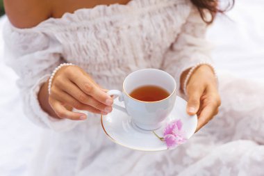 Beyaz dantel elbiseli bir kadının hassas elleri çay fincanı ve çay fincanı tutuyor. Güzellik, zarafet, sağlık ya da sabah çayı yaşam tarzı teması için mükemmel..