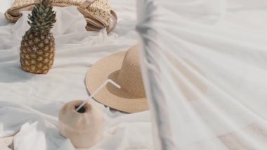El yapımı çadır, ananas, hindistan cevizi içeceği, hasır şapka ve beyaz bir battaniyeye örülmüş bir çantanın olduğu şık bir sahnenin yavaş çekim sahnesi. Seyahat ya da yaşam tarzı görselleri için mükemmel. 