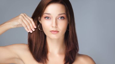 Kusursuz derisi, pürüzsüz düz saçları ve stüdyoda poz veren altın halka küpeleri olan kendine güvenen beyaz bir kadın. Cilt bakımı, güzellik, saç bakımı ve modern moda promosyonları için ideal..