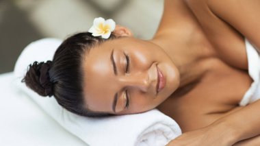 Kaplıcada, yumuşak, parlak bir teni ve kulağının arkasına saklanmış bir çiçekle uzanmış genç bir kadının huzur dolu sahnesi. Sağlık, cilt bakımı, yüz bakımı ve rahatlama hizmeti promosyonları için ideal.. 