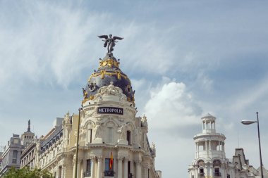 Madrid 'in ikonik Metropolis Binası' na yakın çekim. Süslü mimarisi, siyah kubbesi ve parlak gökyüzüne karşı kanatlı heykeli. Seyahat, editoryal, mimari ve kültürel içerik için ideal.