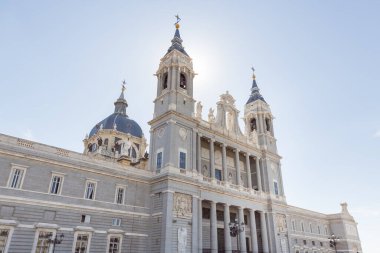 Madrid, İspanya 'daki Almudena Katedrali' nin çarpıcı manzarası, yukarıda mavi gökyüzü ve ikiz kulelerinin arkasında güneş ışığı parlıyor. Seyahat, din, editoryal ve mimari stok kullanımı için ideal.