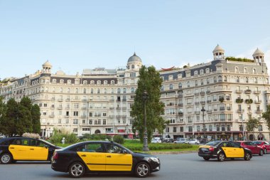 İspanya 'nın Barselona kentindeki sokak manzarasında ikonik sarı-siyah taksiler ve zarif tarihi binalar yer alıyor. Seyahat reklamları, editoryal kullanım, turizm tanıtımı ve Avrupa şehir kavramları için ideal.