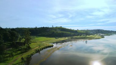 Gregory Gölü 'nün sakin yansıtıcı sularından Nuwara Eliya' nın yemyeşil çay tarlalarına sorunsuz bir insansız hava aracı geçişi. Seyahat, turizm ve ekoloji merkezi görüntüleri için ideal.