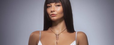 Gösterişli siyah saçlı, beyaz bir elbise ve kolye takmış zarif bir kadın. Moda yazıları, lüks reklamlar ve lüks yaşam tarzı kavramları için idealdir..