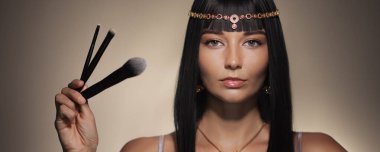 Makyaj fırçaları tutan, zarafet ve güzellik sergileyen Kleopatra 'dan esinlenilmiş muhteşem bir kadın. Güzellik ve kozmetik afişleri için mükemmel. Lüks, sofistike ve zamansız cazibeyi vurgulamak için..