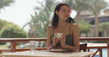 Yeşil mayo giymiş bir kadın, tropik manzaralı bir otel balkonunda elinde kahve fincanı tutuyor. Seyahat, rahatlama ve yaşam tarzı temaları için mükemmel. Promosyon kullanımı için yüksek kaliteli görüntüler. 