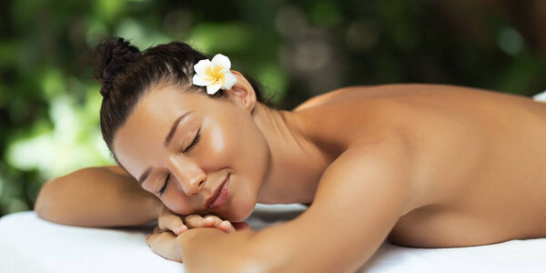 Tranquil Asian woman resting face down on massage table with frangipani flower in her hair and glowing skin. High quality wellness and spa image perfect for beauty and skincare branding.