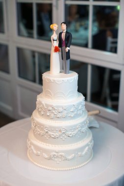 Süslü süslemelerle süslenmiş, üzerinde gelin ve damat figürleri olan çok katlı güzel bir düğün pastası. Evlilik, kutlama, etkinlik planlama ya da romantik etkinlikler için mükemmel..