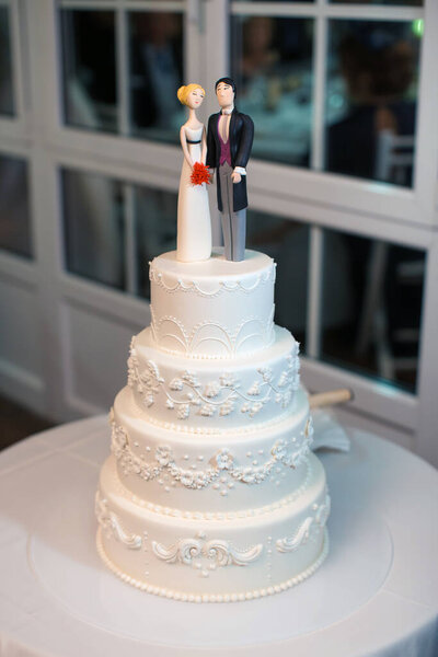 Beautiful multi-tiered white wedding cake decorated with ornate icing and topped with cartoon bride and groom figurines-perfect for marriage, celebration, event planning, or romantic occasion visuals.