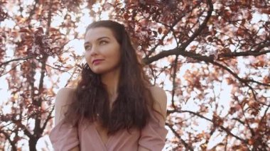 Kiraz çiçekli bir ağacın altında duran, kendine güvenen, kırmızı elbiseli bir kadının yavaş çekim hareketi. Güzellik, moda, mevsimlik reklamlar ve romantik yaşam tarzı içeriği için ideal..