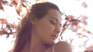 Zarif genç bayan, rüya gibi yumuşak odak noktasında kiraz çiçeklerinin tadını çıkarıyor. Yavaş çekim portresi cilt bakımı, güzellik, parfüm reklamları ve romantik bahar hayat tarzı reklamları için idealdir..