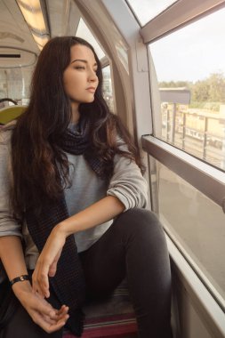 Paris 'te uzun siyah saçlı güzel bir kadın trenin camından dışarı bakıyor. Kavramsal seyahat fotoğrafı, yaşam tarzı, turizm, reklam ve yüksek kaliteli editoryal kullanım için mükemmel.