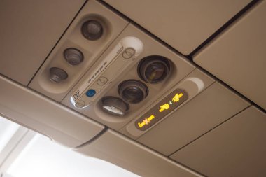 Üst taraftaki uçak panelinde ışıklı emniyet kemeri ve havalandırma ve ışık düğmelerinin yanında sigara içilmediğini gösteren işaretler var. Havayolu güvenliği, seyahat yazıları ve havacılık içeriği için ideal.