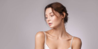 Beyaz tenli, kibar ifadeli, gri arka planda hafif bir ışık olan beyaz bir kadının son moda stüdyo portresi. Lüks güzellik kampanyaları, cilt bakımları ve markalaşma için mükemmel..