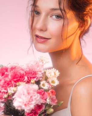 Elinde karanfil ve papatya buketi tutan genç bir beyaz kadının dikey portresi. Çiçek güzelliği, cilt bakımı, sağIık ya da romantik hayat tarzı reklam kavramları için mükemmel..