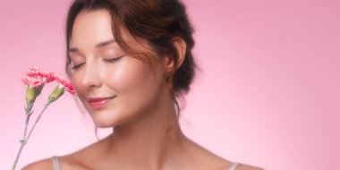 Makyajı yumuşak, gözleri kapalı, pembe karanfil kokusu alan beyaz bir kadın. Sağlık, güzellik, cilt bakımı veya parfüm reklamı için idealdir..