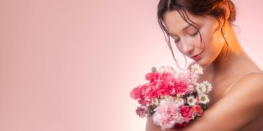 Canlı bir çiçek buketini kucaklayan genç bir bayrağın geniş formatlı güzelliği. Yumuşak pembe tonlar ve hafif ışıklandırma cilt bakımı ve çiçek kampanyaları için mükemmel bir romantik ve zarif görünüm yaratır..