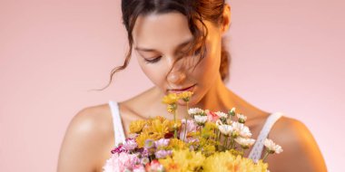 Serene genç kadın elinde parlak bir buket bahar çiçeği gözleri kapalı ve yumuşak bir gülümsemeyle. Güzellik, parfüm, cilt bakımı reklamları ya da romantik yaşam tarzı kampanyaları için mükemmel..