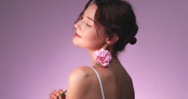 Göz kamaştırıcı bir kadın, omuzunda yumuşak pembe bir karanfil dururken arkasına bakıyor. Koku, cilt bakımı, romantik görseller ve zarif güzellik ürünleri promosyonları için ideal.. 