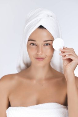 Havlu giymiş zarif genç bir kadın güzellik hizmetleri için yüzüne pamuk tutuyordu. Parlak cilt ve sağlıklı yaşam tarzı. Güzellik ürünleri reklamları, cilt reklamları ve spa reklamları için ideal..