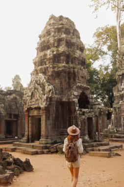 Kamboçya, Angkor 'daki eski Ta Prohm tapınağını araştıran sırt çantalı ve şapkalı bir kadın gezgin. Seyahat, macera, turizm, yaşam tarzı ve kültürel miras tanıtım kavramları için ideal.