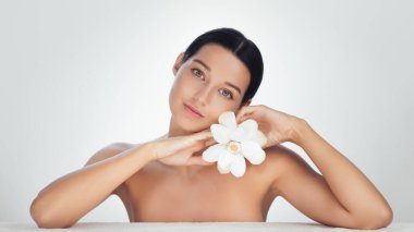 Zarif bir kadın, doğal güzellik ve cilt bakımını sembolize eden beyaz bir çiçek tutar. Sağlık, kaplıca tedavisi, güzellik ürünü reklamları ve lüks cilt bakımı için ideal..