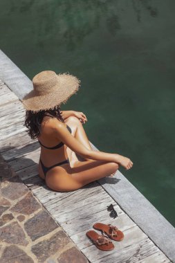 Bikini ve hasır şapkalı, havuz kenarında oturan sandaletli ve güneş gözlüklü bir kadın. Lüks seyahat, kaplıca, moda, yaşam tarzı ve yaz tatili için mükemmel kaliteli stok görüntüleri.