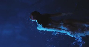 Yüksek kalite şehvetli bir görüntü, bir kadının gece, yukarıdan çekilmiş, parlayan mavi bir havuzda zarif bir şekilde yüzüşünü gösteriyor. Lüks, gece hayatı, uygunluk ve duygusal yaşam tarzı kavramları için idealdir..