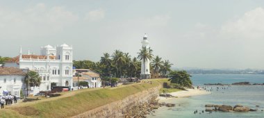 Galle Kalesi deniz feneri Sri Lanka kıyısındaki tarihi koloni binalarının yanında duruyor. Palmiye ağaçları ve okyanusla çevrili bu güzel manzara seyahat ve turizmi desteklemek için idealdir.
