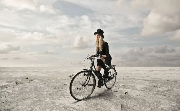 头戴高帽的年轻女子骑着自行车在沙漠中旅行 — 图库照片