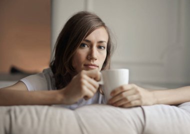 Elinde bir bardakla koltukta oturan genç bir kadının portresi.