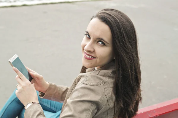ベンチに座っている若い女性はスマートフォンを使って — ストック写真