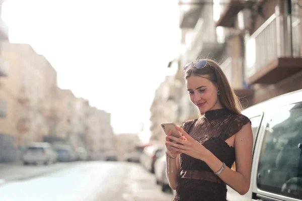 エレガントな若い女性が路上でスマートフォンを使い — ストック写真