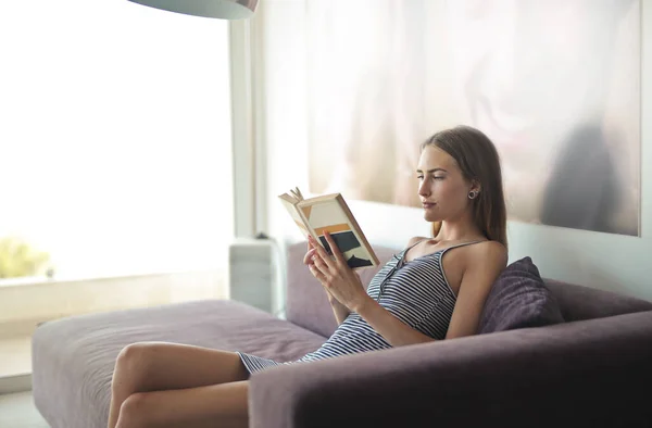 年轻女子在沙发上看书 — 图库照片