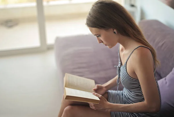 Μια Νεαρή Γυναίκα Διαβάζει Ένα Βιβλίο Στον Καναπέ — Φωτογραφία Αρχείου