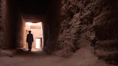 Mhamid, Fas 'taki Kasbah' ın içinde mavi gandoura ve türban giyen geleneksel giyimli bir Bedevi adam yürüyor. Güney Fas 'ın otantik kırsal manzarası. 4k.