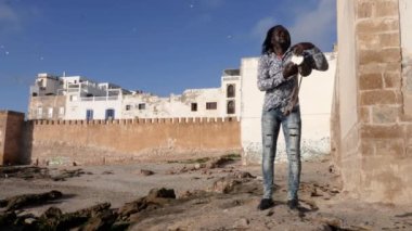 Afrika perküsyon müziği, Senegalli bir adam sopayla geleneksel bir dun davulu çalıyor. Essaouira, Fas plajında sokak müziği. 4k