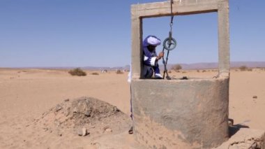 Geleneksel olarak giyinmiş Faslı bir bedevi Gandoura giyer ve türban Fas 'ın Sahra Çölü' nde kurak bir kuyuda su arar. İklim değişikliği kavramı, çevre sorunları, Fas 'ta kuraklık. 4k görüntü