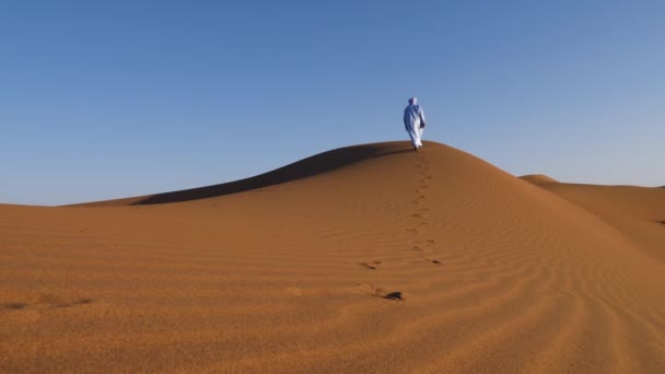 伝統的に青いガンダラ ジデラバ ターバンを着たモロッコ人男性が砂丘 人間のチガガ砂漠 モロッコを歩いています 南モロッコの本格的な砂漠のシーン 4Kについて — ストック動画