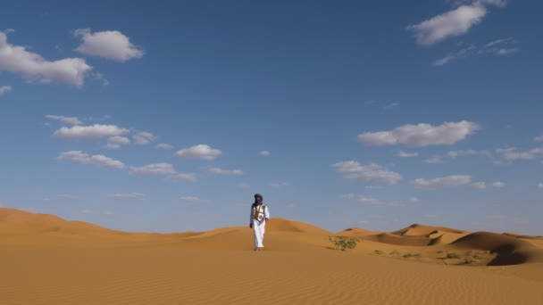 在摩洛哥的Erg Chebbi沙漠 一名身穿白色长袍 头戴杰拉巴和头巾的传统摩洛哥男子走在沙丘上 摩洛哥南部真正的沙漠景象 — 图库视频影像