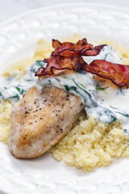 Ispanak kremalı tavuk göğsü ve kuskus ile servis edilen domuz pastırması.