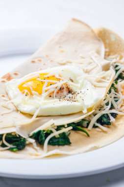 Kızarmış yumurta ve rendelenmiş peynirle servis edilen ıspanak yapraklarıyla doldurulmuş krep.